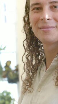 Vertical video: Crop shift, turning person in tan top greeting camera by window, plants, copy space