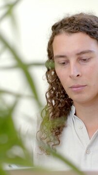 Vertical video: Panning plant into frame obscuring adult in shirt using laptop at desk, copy space