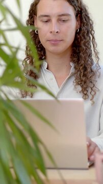Vertical video: Starting work worker in light shirt typing and reading on laptop at home with plant