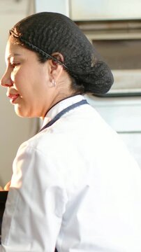 Vertical video: Responding to timer, chef with apron pulling hot tray from oven wearing blue gloves