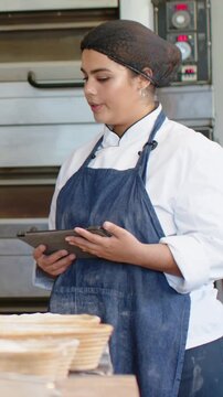 Vertical video: Holding tablet chef in coat motioning checking times at bakery with oven baskets