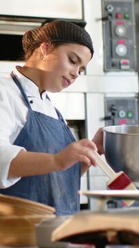 Vertical video: Per recipe baker coat blue apron brushing pastry for oven at bakery with red brush