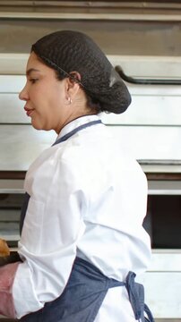 Vertical video: Timer pinging baker holding tray from oven while chef adding jar to rolls in bakery