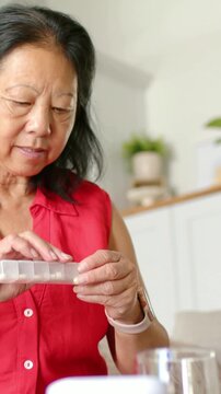 Vertical video: Leaning older woman red top picking pillbox checking doses to take meds with glass