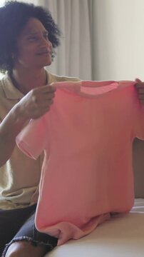 Vertical video: Reaching into box man wearing shirt, pulling pink shirt on bed, inspecting fabric