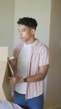 Vertical video: Lifting box man in stripes inspecting box marking with marker for moving at home