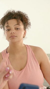 Vertical video: Sipping woman pink top with glass taking phone as hand lifting it, reading at home