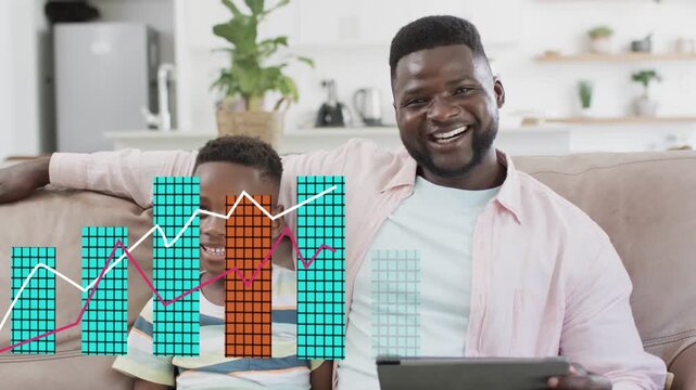 Father and son sitting on couch, tapping tablet and watching growing finance chart teaching savings