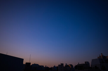 Naklejka premium Minimalist view of a city skyline at dusk, featuring a beautiful deep blue gradient sky transitioning into soft orange and purple hues near the horizon.