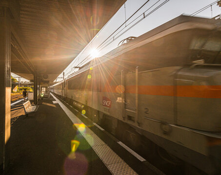 San Sebastian, Spain - July 28 2016: Fast passenger train passing station platform in golden sunlight.