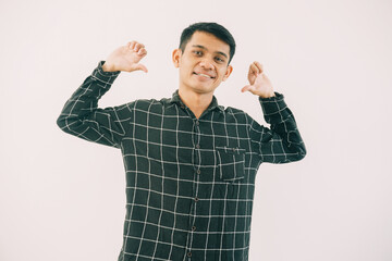 Naklejka premium young asian male wearing dark green and black checkered long-sleeve shirt, hands raised in peace sign. bright even lighting with clean white background ideal for advertising and social media content.