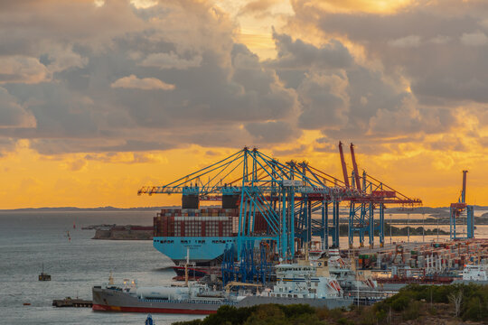 Gothenburg, Sweden - August 24 2020: Container port cranes loading cargo ships at dramatic sunset.