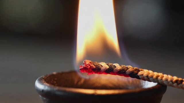 Close-up of a lit agarbatti stick in a small metal holder with a warm flame and dark background.