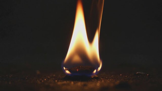 Close-up of a small flame burning on a dark surface with warm lighting