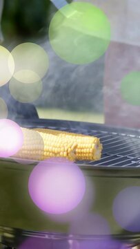 Vertical video: Two men handling tongs placing second corn on grill, smoke rising, cooking barbecue