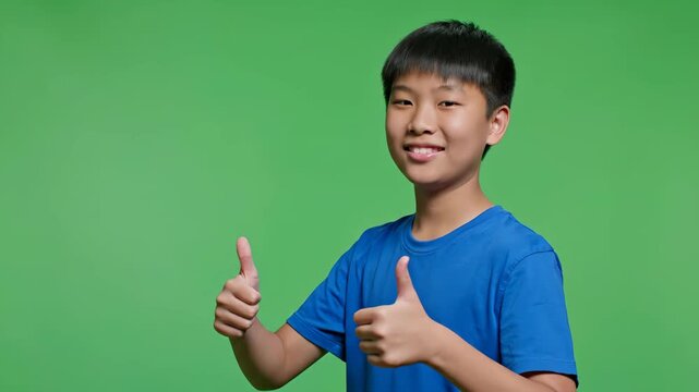 A cheerful Asian boy expresses approval and success with a confident double thumbs up gesture. He is smiling broadly, conveying positivity and agreement.