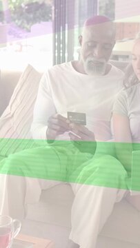 Vertical video: Senior couple sitting on sofa, man reaching for card and verifying payment on phone