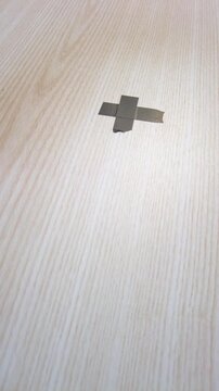 Closeup of tripod foot near tape marking on wooden surface. Detailed view of tripod foot placement next to taped cross on light wood floor indicating stable setup