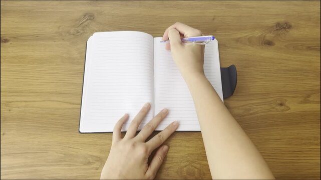 Close-up video of a person writing in a notebook. Hand holding a pen and taking notes on paper, representing work, study, planning and productivity in a calm indoor setting.