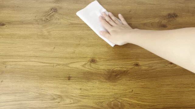Close-up video of a hand wiping a table surface with a paper napkin. Cleaning process in a home environment, representing hygiene, cleanliness and daily routine.