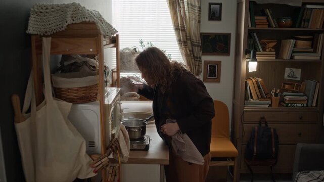 High angle shot of woman cooking on portable stove in small kitchen in poor, run down studio apartment