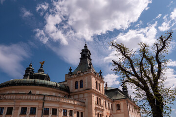 Obraz premium Historic Reduta building in Spišská Nová Ves with tower and dome under dramatic sky, complemented by a spring tree.