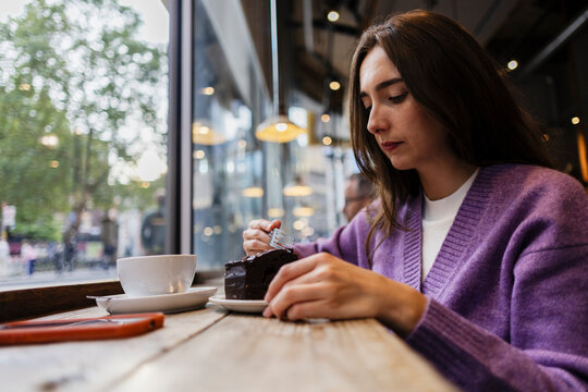 Woman enjoying chocolate cake and coffee in a city cafe window