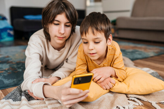 Brother playing on a smartphone with a sibling indoors