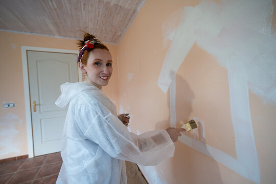 Smiling homeowner painting house outline on indoor wall