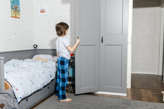 Child in pajamas opening wardrobe in bedroom for morning routine