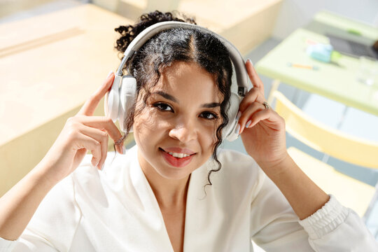Smiling woman holding headphone looking at camera indoors