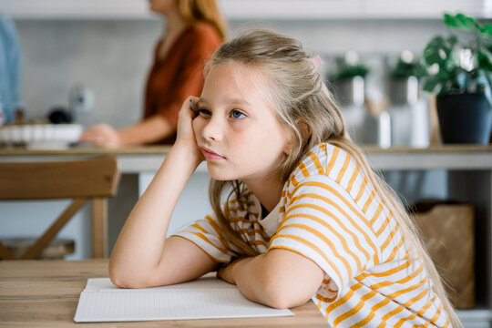 Bored child sitting at table with notebook thinking about homework