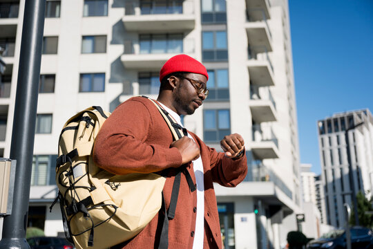Man wearing backpack checking watch on urban street in casual clothes