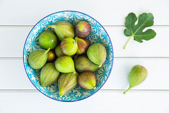 Fresh green figs in a patterned bowl on a white wooden table