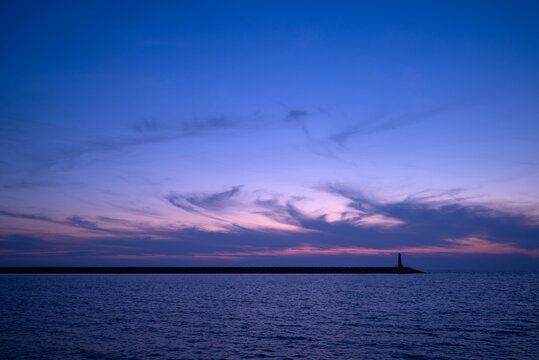 Lighthouse on horizon during blue hour over calm sea