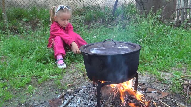 Child by Fire, Cooking at Fireplace in a Pot for Eating, Rustic Kid, Girl in Yard, Countryside