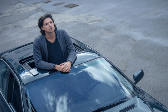 Contemplative man standing through sun roof of car