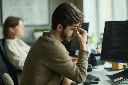 Tired programmer rubbing eyes while working at the office desk