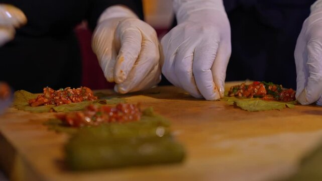 Close-up of a team preparing stuffed grape leaves with olive oil, showcasing traditional Turkish cuisine, teamwork in the kitchen, and handmade food preparation with fresh ingredients.