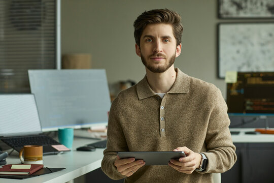 IT professional holding tablet at office desk looking at camera