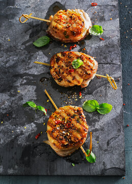 Grilled pork medallions on skewers with basil and chili on slate
