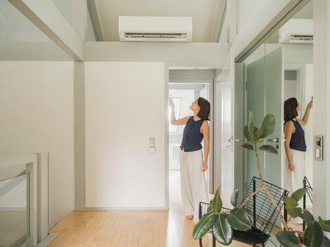 Woman using air conditioning with remote control in modern home