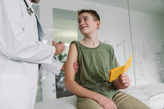 Smiling teenage boy receiving vaccination from doctor at the clinic