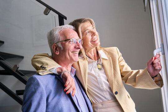 Smiling couple embracing by the window at home enjoying happiness