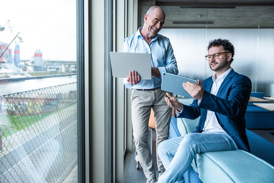 Smiling coworkers using digital devices during an office meeting