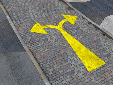 Yellow diverging arrow painted on cobblestone street
