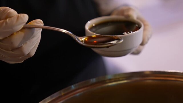 Close-up of thick pomegranate molasses held in a spoon, slowly dripping with a glossy texture. The rich dark color and viscosity highlight a traditional ingredient used in Middle Eastern and Mediterra