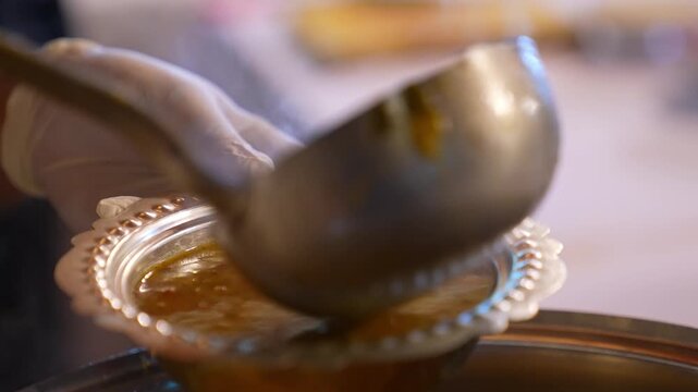 Close-up of hot soup being served into a bowl with a ladle, showing final serving stage, rich texture, and traditional homemade food presentation in a kitchen setting.