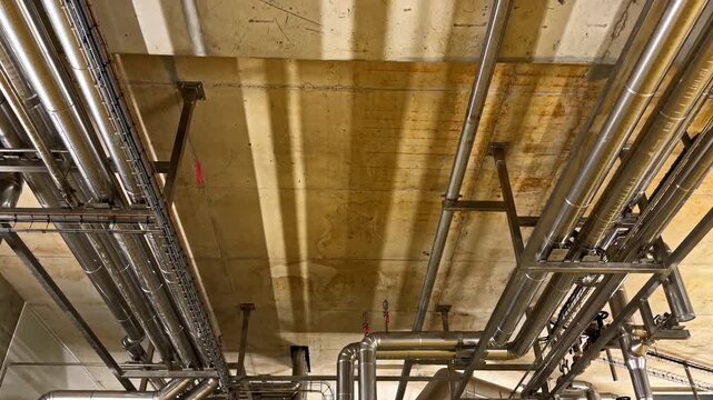 Stainless steel pipes run parallel across a concrete ceiling, highlighting industrial design. Ideal for illustrating infrastructure or architectural details.