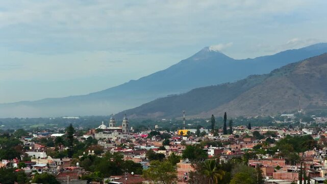 Aerial flyover of Tuxpan cityscape with snowed Colima volcano in the background, Mexico